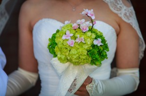 A bride in a lace dress holding a bouquet of wedding flowers with pink blossoms.