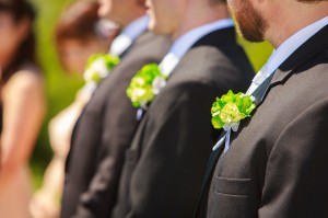 Groomsmen lined up at a wedding, wearing dark suits with green floral boutonnieres for perfect wedding photography.