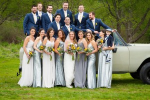 Kristen and Tim's wedding party posing outdoors at Crissey Farm; group of men in blue suits and women in different shades of grey dresses, holding yellow bouquets, with a vintage car