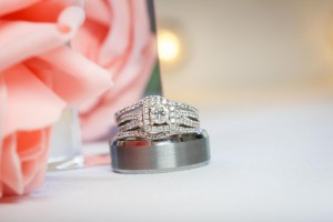 Close-up of a diamond engagement ring stacked on a wedding band, captured by Easthampton Wedding Photography, with soft focus on a pink rose in the background.