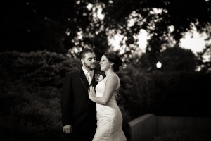 A bride and groom, Heidi and Tom, embracing and smiling at each other in a garden, captured in black and white.