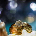 Close-up of a diamond ring placed on top of gold wedding bands at Lord Jeffery Inn, set against a softly blurred blue background with light bokeh.