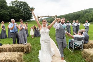Bride and Groom holding hands in the air as they are walking down the aisle after ceremony with parents and wedding party clapping in the background