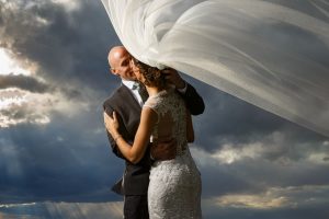 Bride and Groom with brides veil blowing in the wind with ominous sky behind them