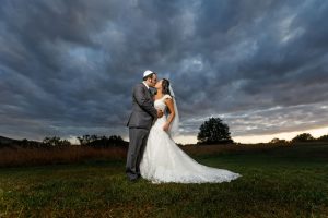 Groom with yamaka kissing bride in field with dramatic sky in background