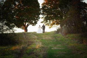 Bride and Groom walking away up trail between two trees with skyline behind them