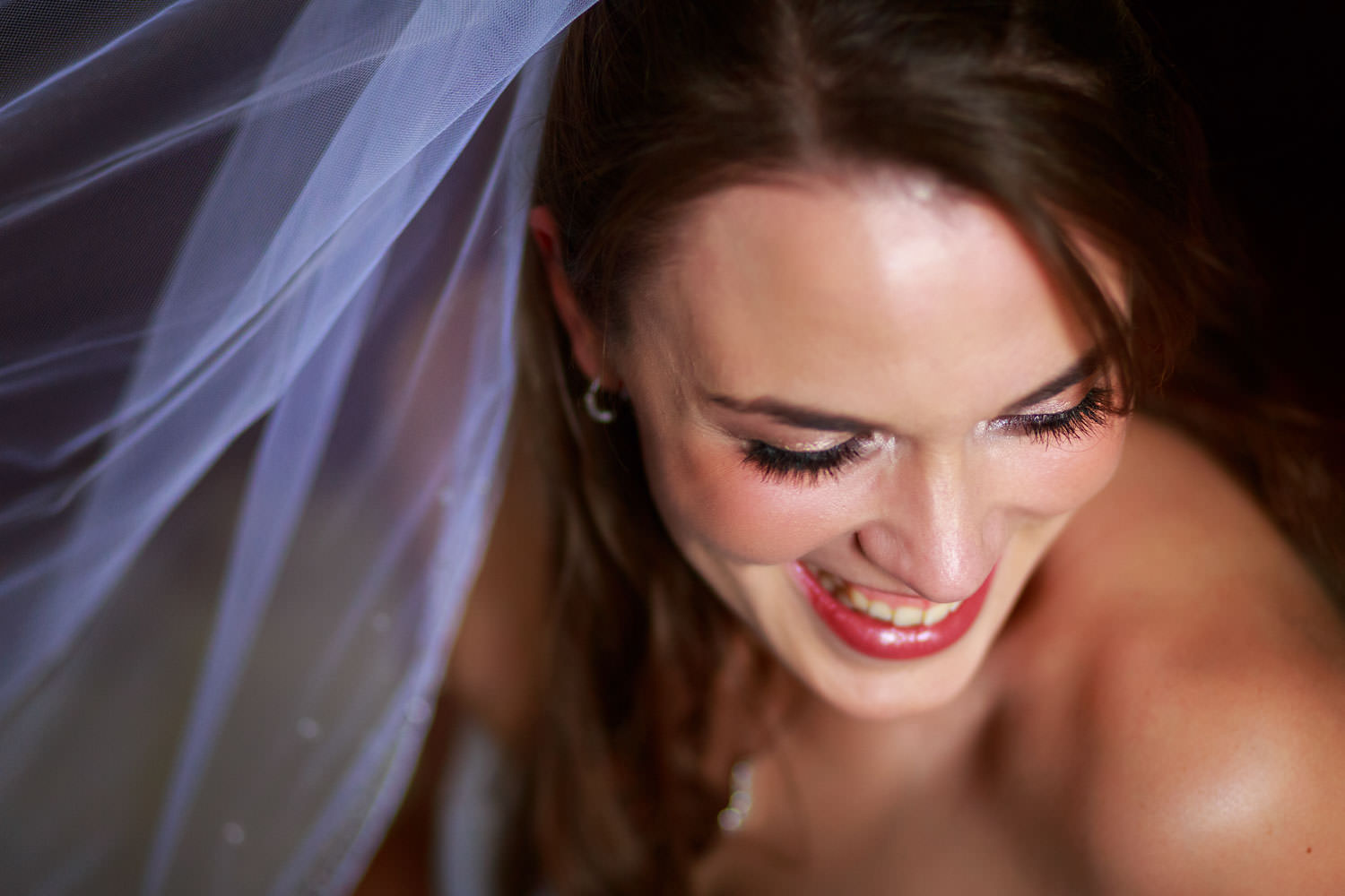 Wedding day portrait of a happy smiling bride. The veil in the background with soft window light streaming onto the bride