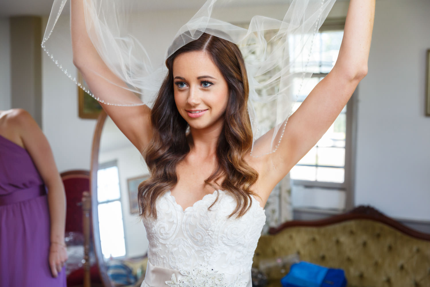 Bride playing with her veil in front of the mirror in the bridal suite. Acting playful and smiling