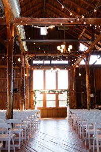 empty ceremony space setup with white chairs inside barn