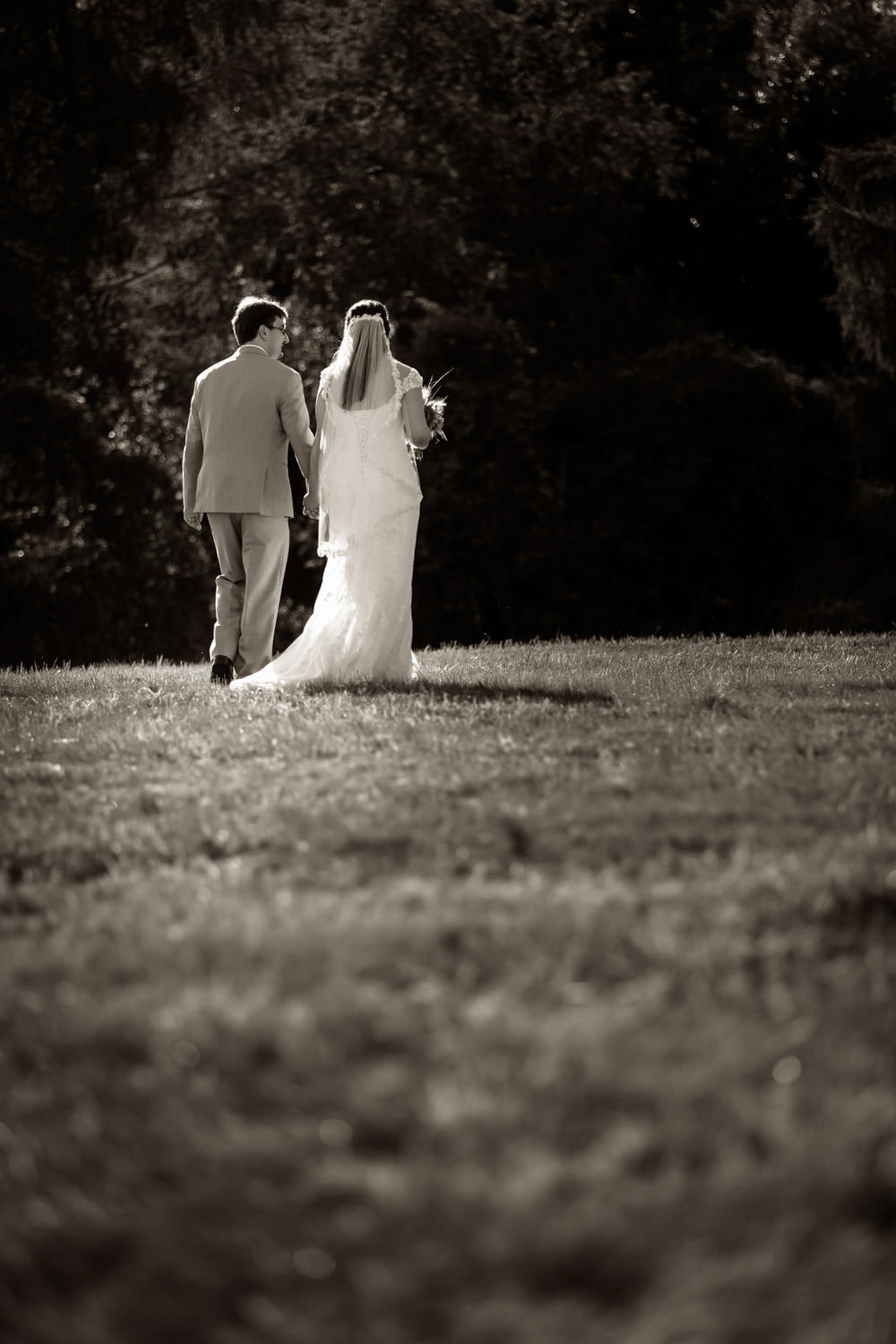 Black and White photo of the bride and groom walking away in a field at the red barn