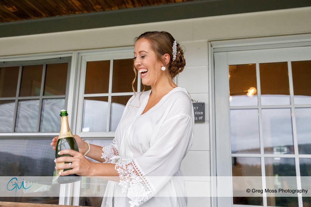 Bride in white robe opening champagne bottle