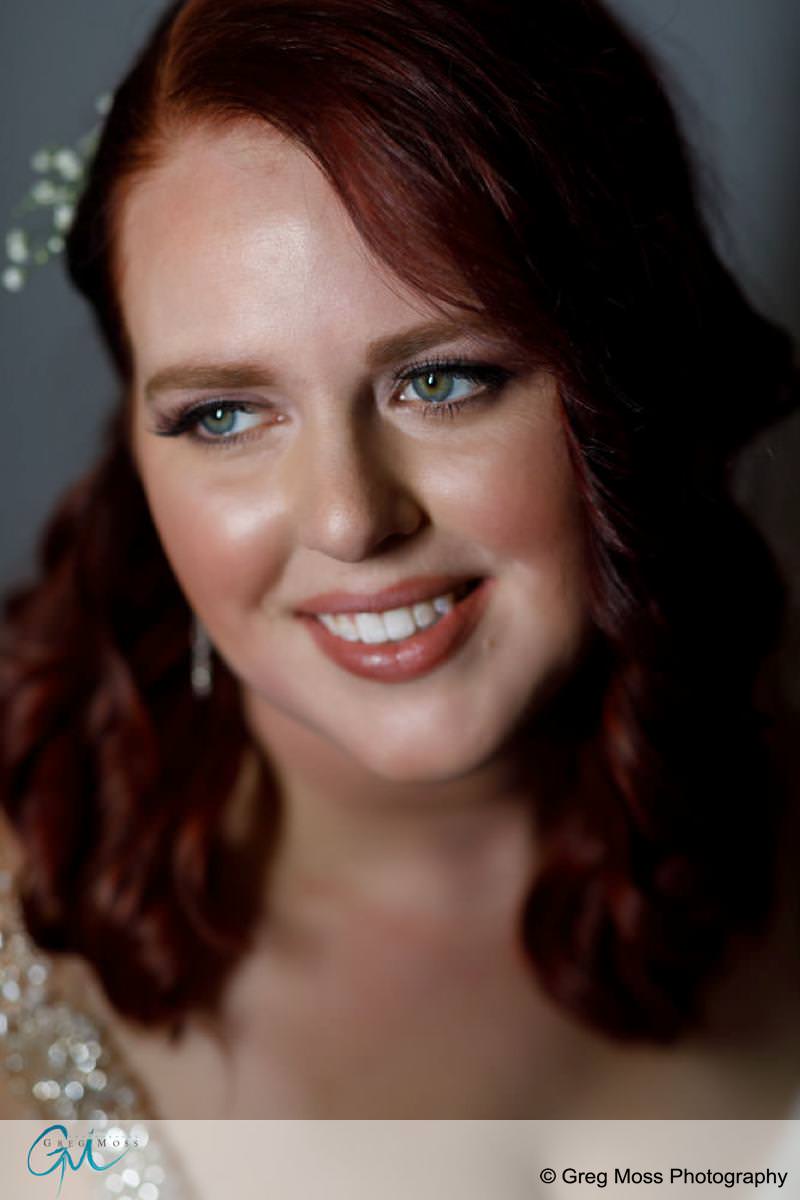 Close-up portrait of a woman with red hair and blue eyes, smiling, wearing a white dress with a decorative hairpiece at a Red Barn Wedding.