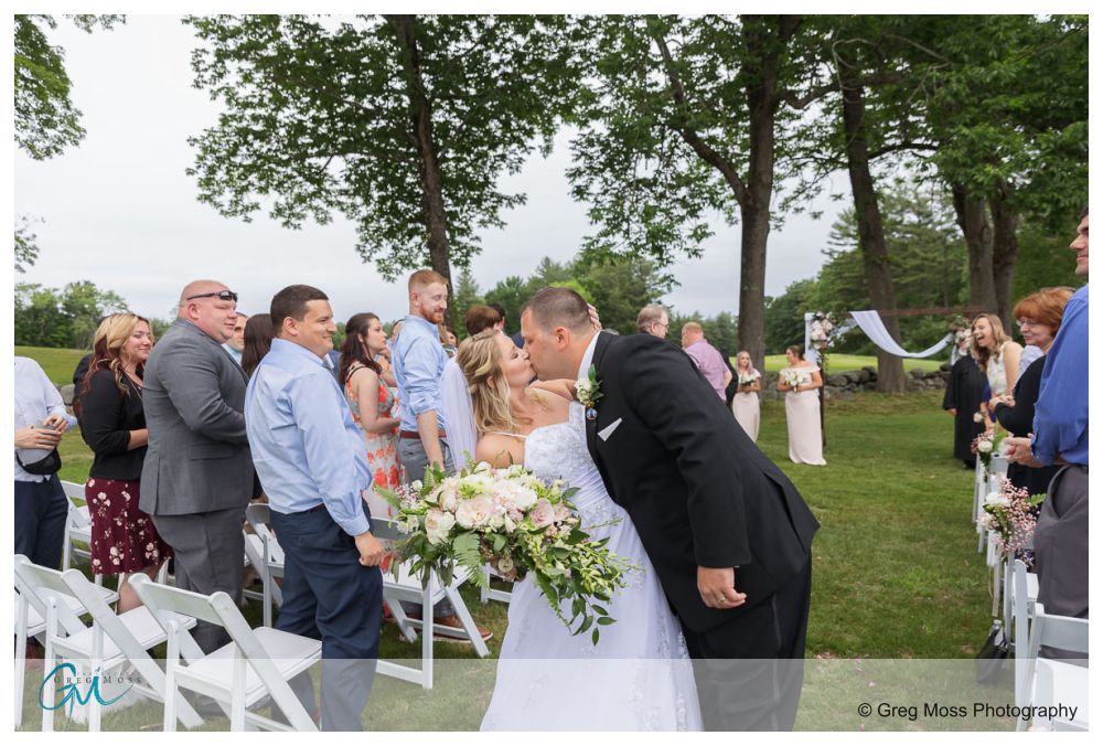Bride and groom kissing in the aisle after ceremony with guests in background