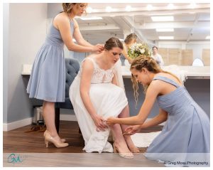 Bridemaids helping bride with shoes and hair