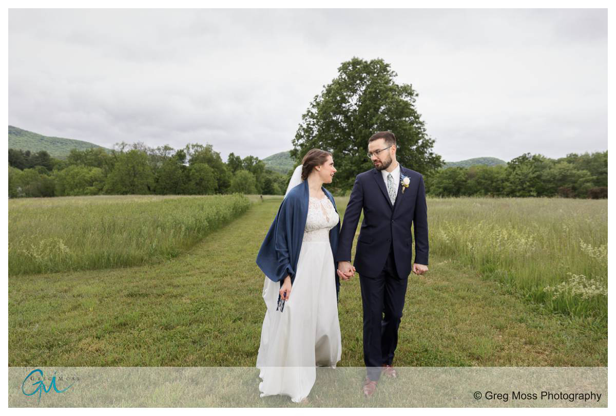 Bride and Groom walking in field in front of big tree at the Red Barn at Hampshire college