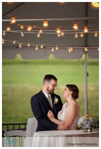 A couple exchanging a loving gaze under string lights at a Hampshire College outdoor wedding reception.