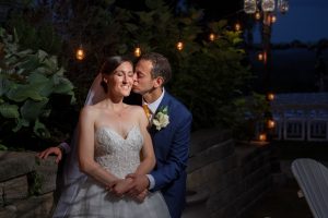 Wedding Photography at The Mountain Rose Inn: A groom kissing a bride on the cheek at night, surrounded by garden lights, with a softly lit gazebo in the background.