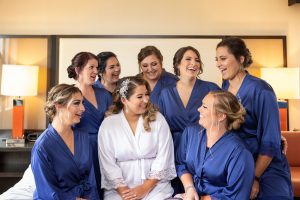 Bride and bridesmaids hugging on bed with matching monogramed robes