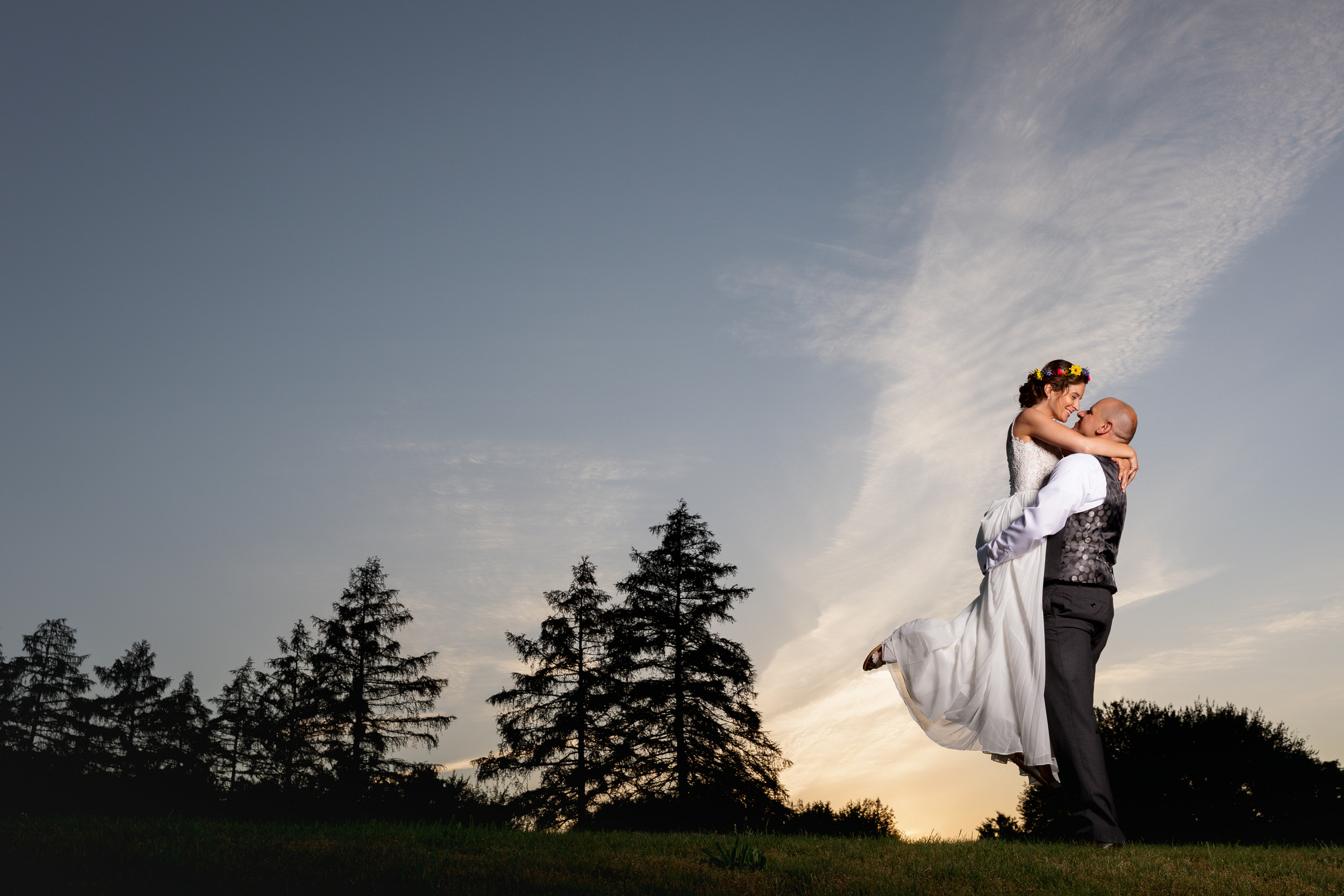 Groom lifting bride with flower headpiece at sunset