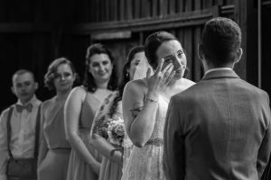 Black and White photo of bride wiping a tear away during ceremony