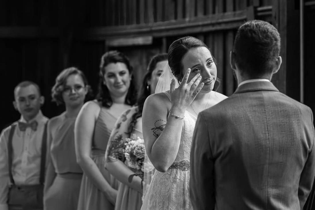 Black and White photo of bride wiping a tear away during ceremony