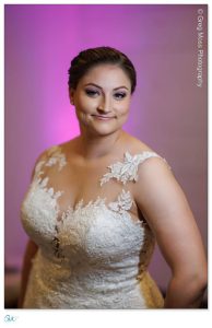 A woman in a detailed lace wedding dress smiling gently against a softly blurred pink background, captured by Holyoke Wedding Photography.