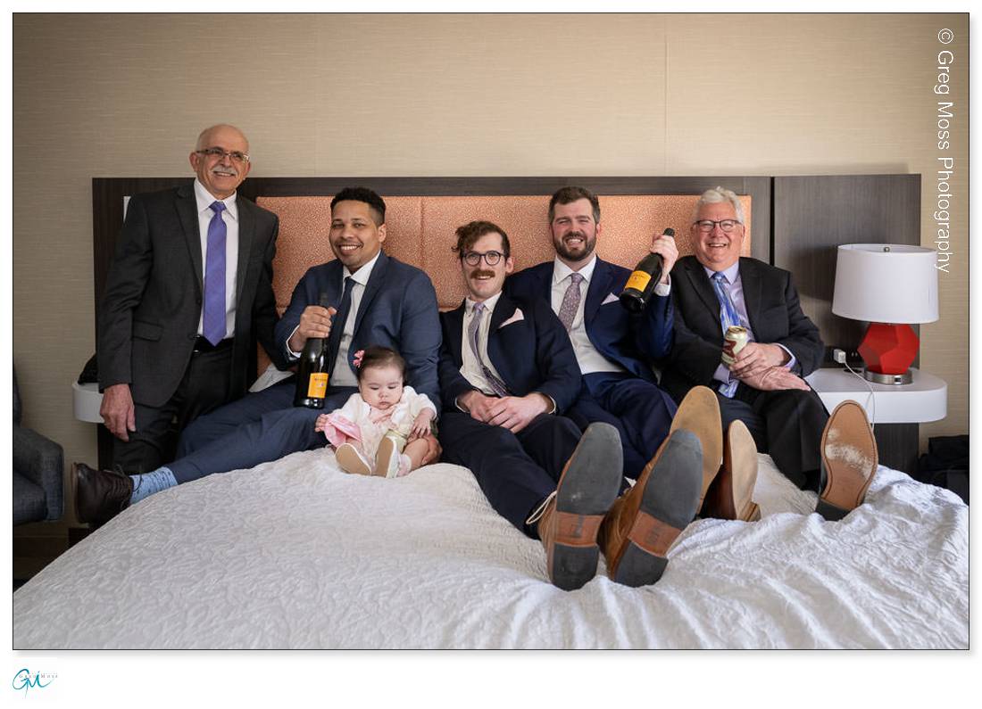 Groom with goomsmen on bed with champagne