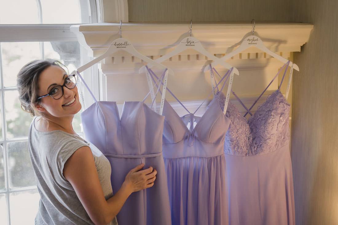 Bridesmaid helping to hang dresses in front of window