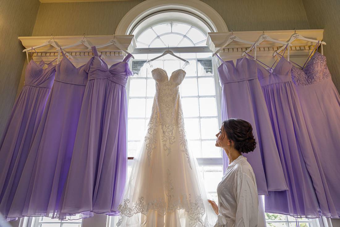 Bride looking at dress hanging in front of window