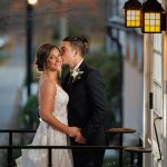 A bride and groom embracing on a balcony, with the groom kissing the bride's cheek under evening lights during their Western MA wedding.