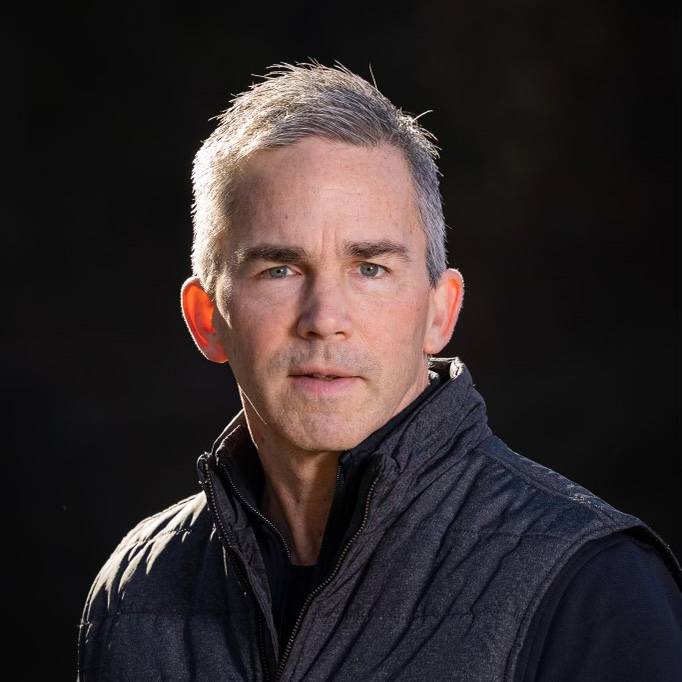 Portrait of a middle-aged man with salt and pepper hair, wearing a black jacket, gazing intently off-camera against a dark background at a Western MA wedding.