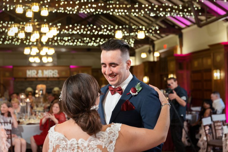 A newlywed couple shares a dance under string lights at a wedding reception in Western Massachusetts, with guests and a "mr. & mrs." sign visible in the background.