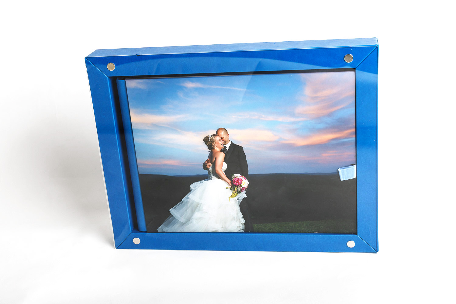 A framed wedding photo of a smiling couple embracing outdoors at sunset, displayed in a blue frame against a white backdrop, perfect for wedding album designs.