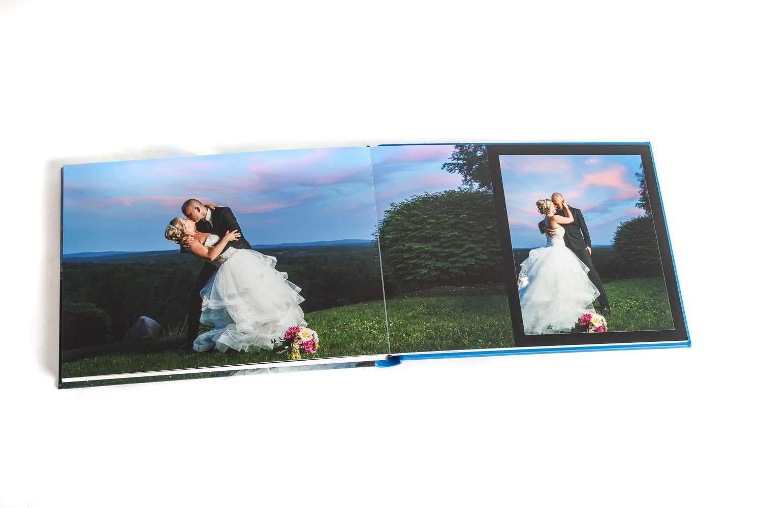 An open wedding album showing a couple embracing outdoors at sunset, displayed across two pages with a scenic backdrop.