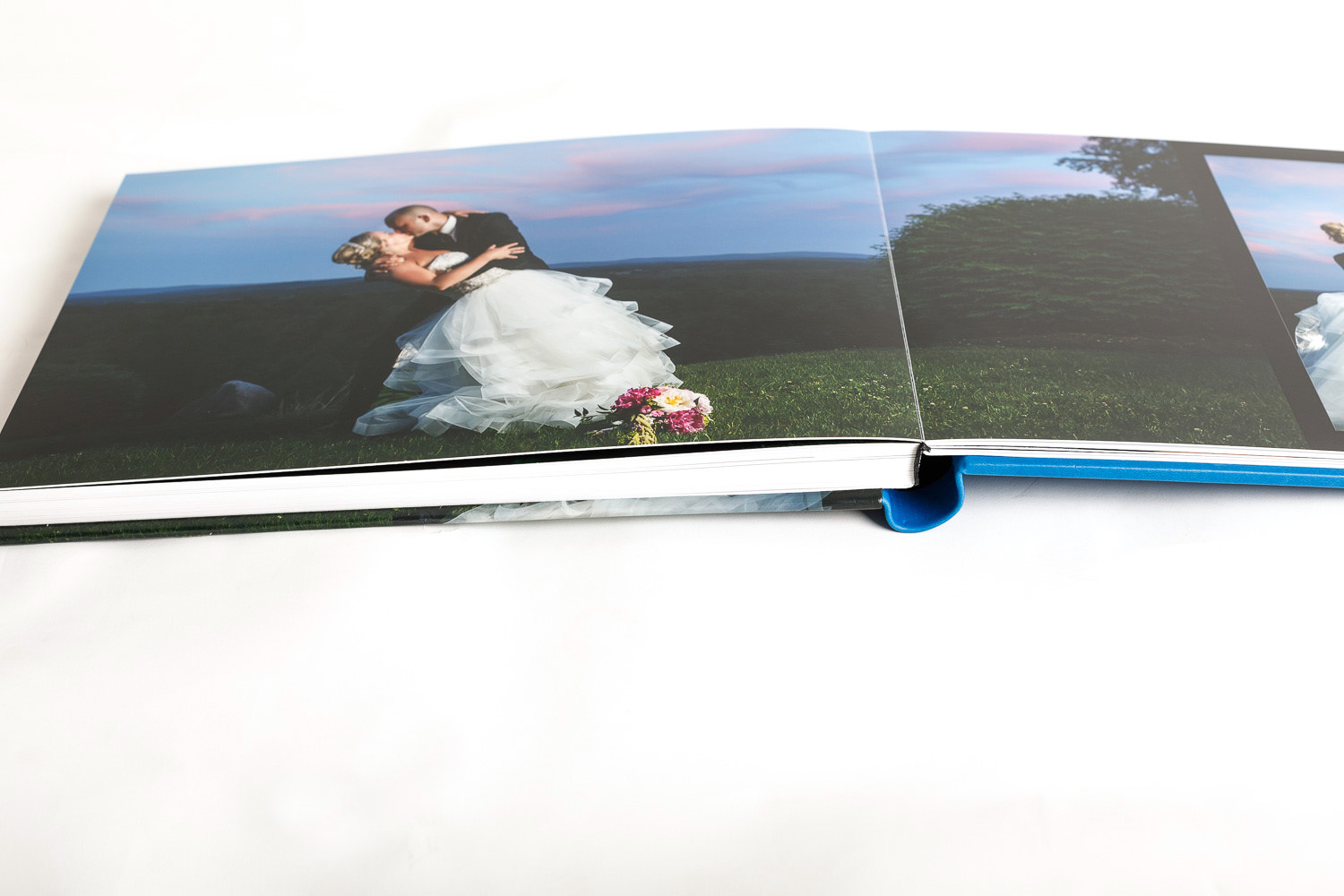 An open wedding album displaying a page with a bride and groom embracing on a grassy field at dusk.